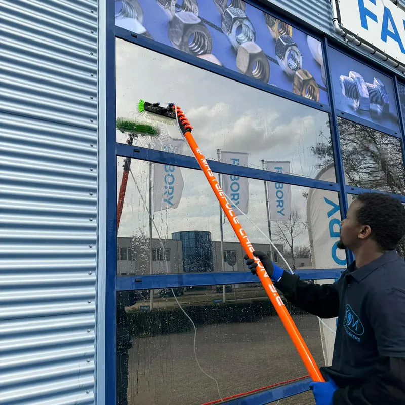 A KM team member cleans a shop window with a telescopic pole.