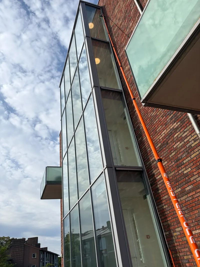 A telescopic brush cleans high windows on a glazed facade.