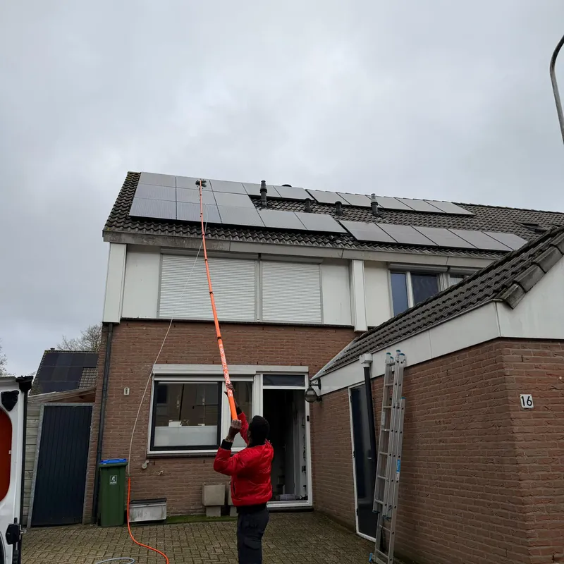 A team member cleans rooftop solar panels with a long telescopic pole.